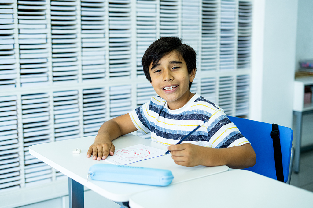 Alumno sentado, sosteniendo un lápiz y sonriendo en el aula de un centro Kumon.